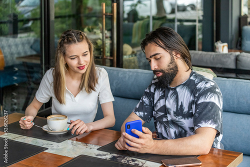 Young couple sitting at the restaurant and girl looking at Man's phone