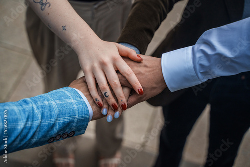 Portrait of business meeting of four people holding their hands together outdoors in city.