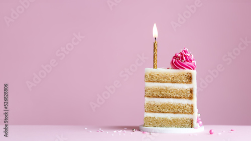 Slice of birthday cake with gold birthday cake candle and pink frosting