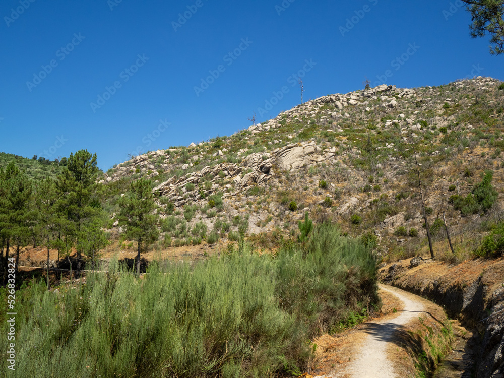 PR10 SEI walking route aside a water channel separating the pine trees forest below and the rocky mountain above in Serra da Estrela, Portugal