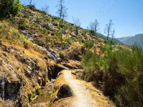 PR10 SEI walking route aside a water channel separating the pine trees forest below and the rocky mountain above in Serra da Estrela, Portugal photo
