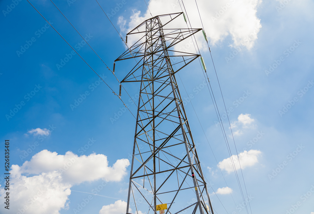 close-up of electricity power pylons and cables against a bright blue summer sky, white cloud close-up of electricity power pylons and cables against a bright blue summer sky, white cloud