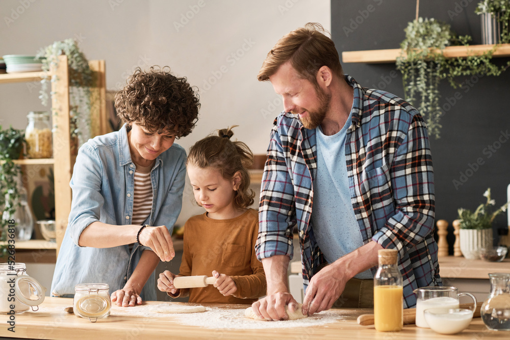 Parents teaching their little son to bake homemade pie from dough at table in kitchen Parents teaching their little son to bake homemade pie from dough at table in kitchen