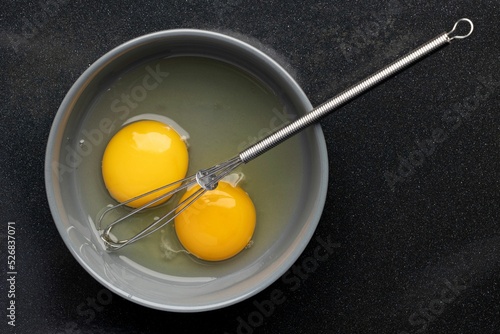 Canvas-taulu Closeup of beaten eggs in a bowl with a whisk on a black table