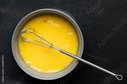 Closeup of beaten eggs in a bowl with a whisk