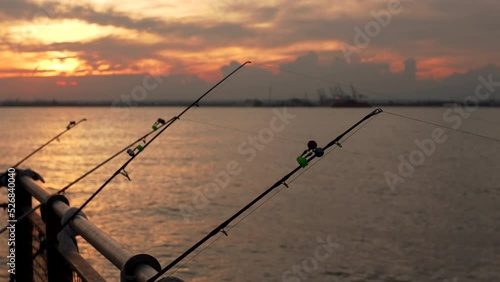 Silhouettes of a few fishing rods against the New York bay water and beautiful yellow sunset. The sky is yellow and orange, the waves reflect bright colors. NYC, USA. Summertime photo