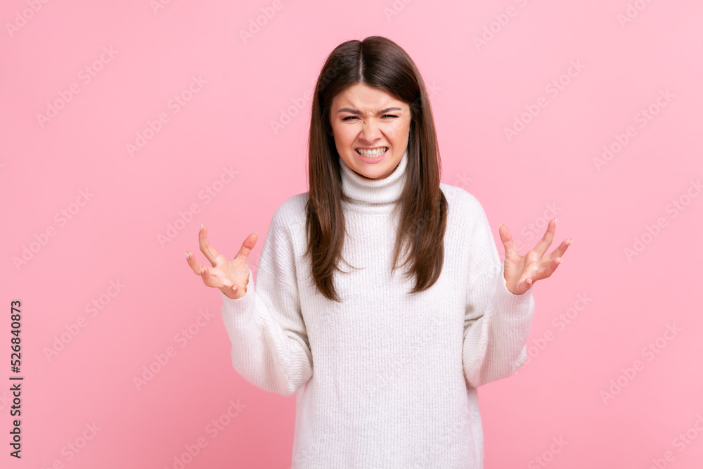 Portrait of angry female standing with raised arms, expressing aggression, screaming, frowning face, wearing white casual style sweater. Indoor studio shot isolated on pink background. Portrait of angry female standing with raised arms, expressing aggression, screaming, frowning face, wearing white casual style sweater. Indoor studio shot isolated on pink background.
