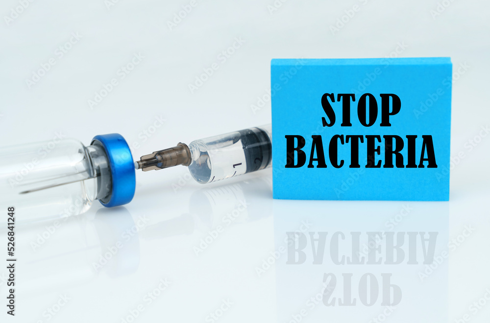 On a white reflective surface there is a syringe with an ampoule and a plate with the inscription - STOP BACTERIA On a white reflective surface there is a syringe with an ampoule and a plate with the inscription - STOP BACTERIA