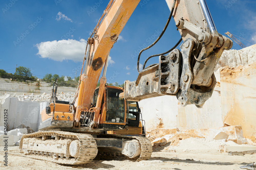 Huge caterpillar construction machine with grabber working on territory of modern production factory situated on marble quarry Huge caterpillar construction machine with grabber working on territory of modern production factory situated on marble quarry