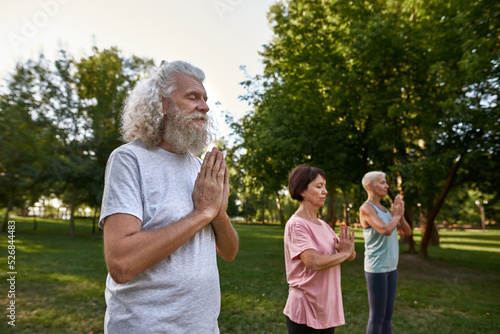Sportive elderly friends meditate with closed eyes