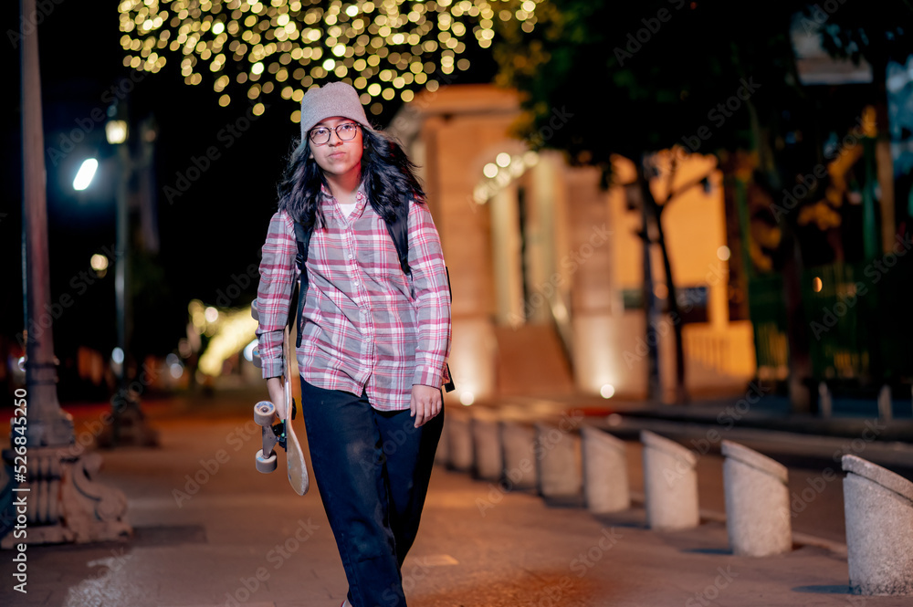 Woman walking on the street at night with her Skateboard.