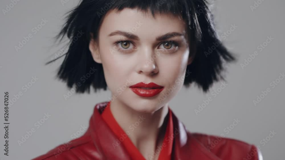 Beauty portrait of a fashion model with beautiful make-up with red lips and in a red cloak moves looking at the camera with her eyes. Beauty portrait of a fashion model with beautiful make-up with red lips and in a red cloak moves looking at the camera with her eyes.
