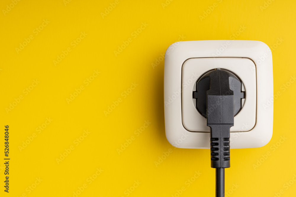 Electric plug and wall socket on yellow wall.