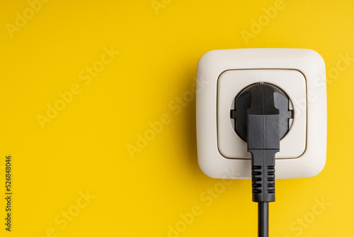 Foto Electric plug and wall socket on yellow wall.