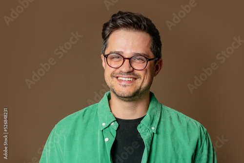 Canvas Print Stylish caucasian man in glasses and green shirt on brown background