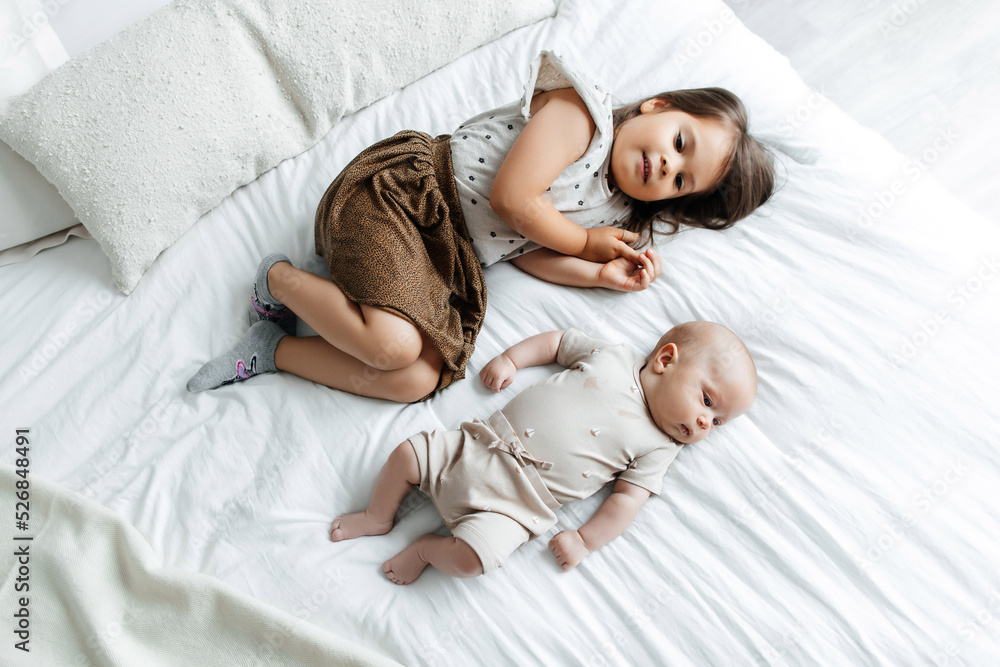Little girl and her newborn brother are lying on the bed in the bedroom, top view. The children are resting on the bed. The children fall asleep in their bedroom Little girl and her newborn brother are lying on the bed in the bedroom, top view. The children are resting on the bed. The children fall asleep in their bedroom