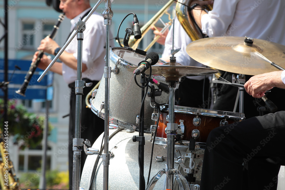 Fototapeta premium A group of professional musicians on stage playing drums and wind instruments into a microphone concert outdoors on a summer day