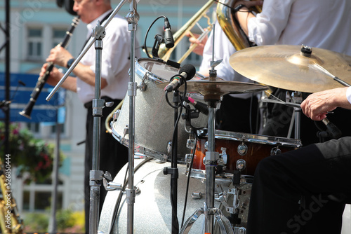 A group of professional musicians on stage playing drums and wind instruments into a microphone concert outdoors on a summer day