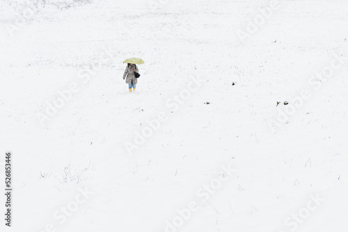 A woman with a yellow umbrella walks down the hill through the snow