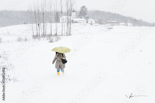 A woman with a yellow umbrella walks down the hill through the snow photo