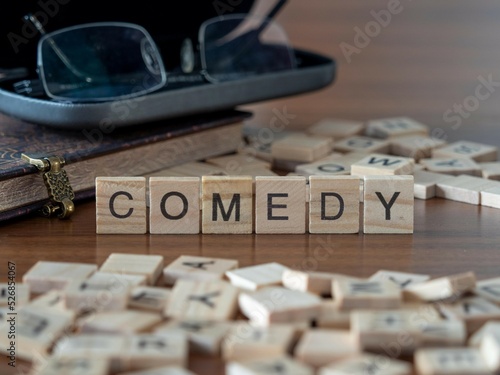 comedy word or concept represented by wooden letter tiles on a wooden table with glasses and a book photo