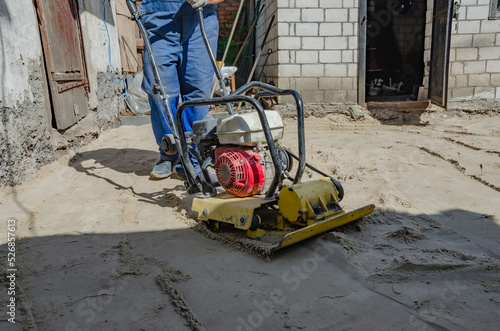 Worker in uniform and knee pads use vibratory plate compactor for path construction.