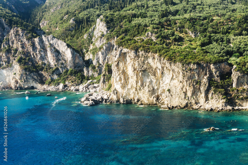 High cliff with the ocean at the bottom. Corfu island - Greece. Clear transparent turquoise sea. Exotic vacation landscape. Forest on a hill. Paleokastritsa scenic view. High summer mountain.