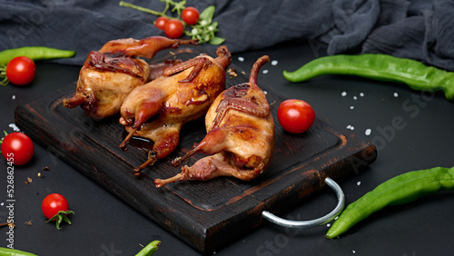 Frying carcasses of quails lie on a wooden board with vegetables, a black table