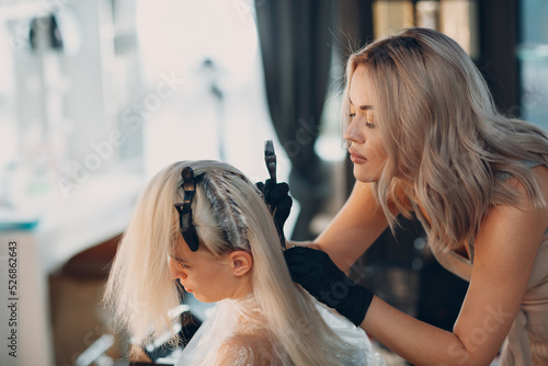 Young woman hairdresser dying hair at beauty salon. Professional hair roots coloring. photo