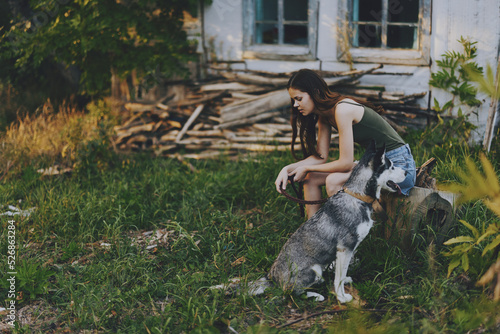 A woman sits near an old house in the village with her husky dog ​​in summer and looks at the sunset