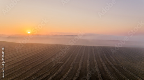 Brown farm field with fog-covered horizon and bright orange rising sun. Colorful morning sky. Landcape of Roztocze Poland. Horizontal shot. High quality photo