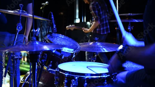 Drummer playing drums at stage, close up. Music concert. Drummer on festival with band under the stage lights. Drummer playing drum kit in nightclub at live rock concert. Music instrument.