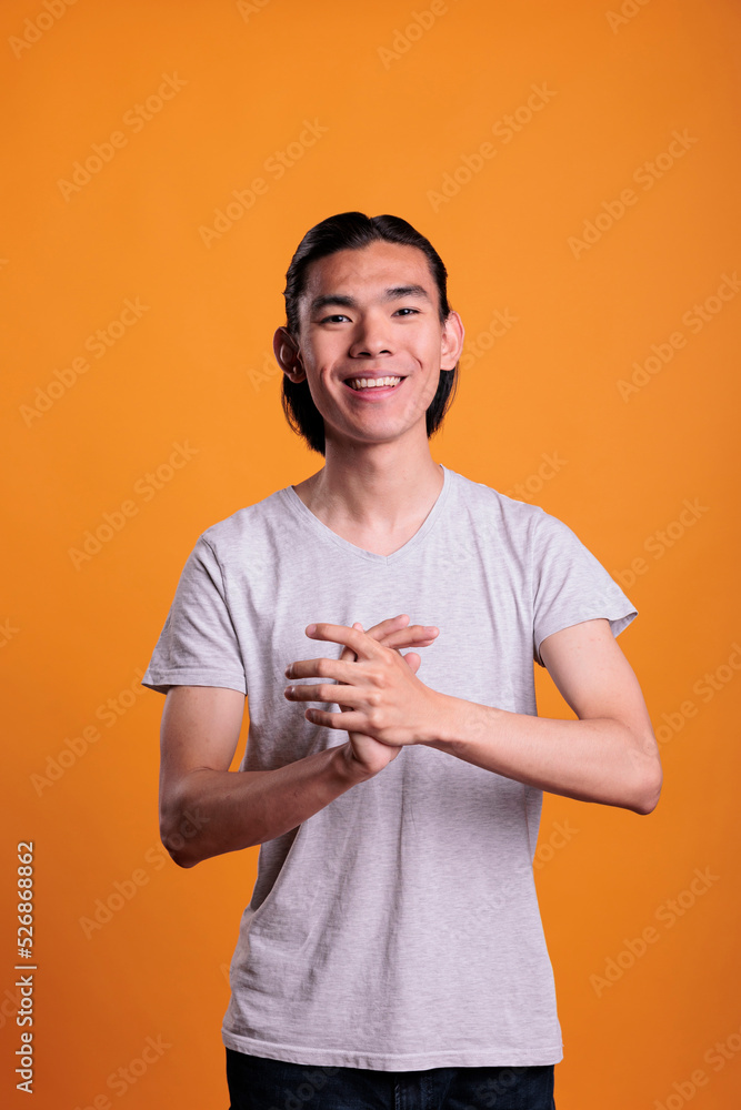 Young cheerful smiling asian man applauding, looking at camera. Positive laughing teenager with joyful facial expression clapping hands, attractive person standing, medium shot portrait Young cheerful smiling asian man applauding, looking at camera. Positive laughing teenager with joyful facial expression clapping hands, attractive person standing, medium shot portrait