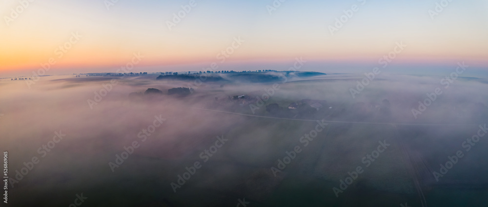 Fototapeta premium Colorful sunrise and thick fog over vast farm fields of Roztocze Poland. Nature and agriculture. Wide horizontal shot. High quality photo