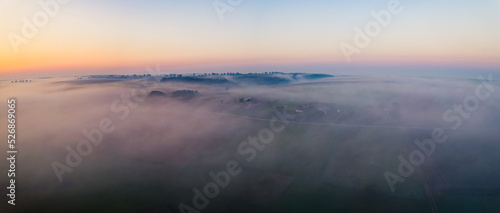 Colorful sunrise and thick fog over vast farm fields of Roztocze Poland. Nature and agriculture. Wide horizontal shot. High quality photo