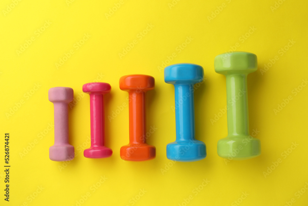 Many different stylish dumbbells on yellow background, flat lay Many different stylish dumbbells on yellow background, flat lay