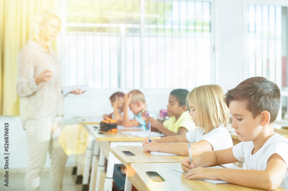 Fototapeta premium Group of preteen schoolchildren diligently working in class, making notes of teacher lecture