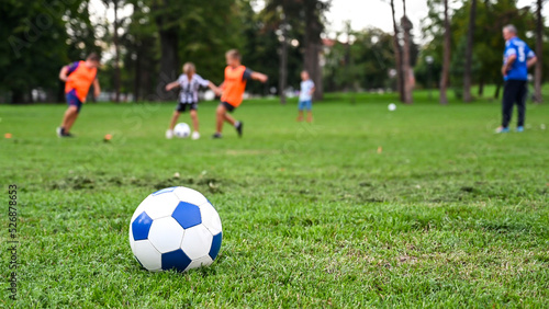 Children playing football in the park. Ball in foreground while boys are playing in the background on green grass. Happy and cute children having football match on stadium. Football soccer match.