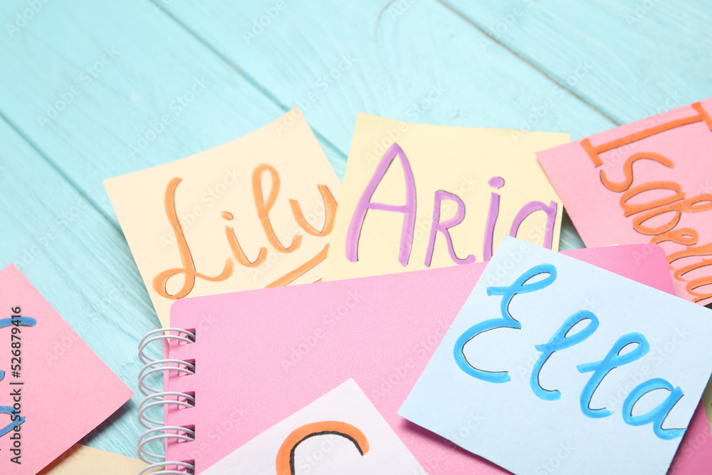 Paper notes with different baby names and notebook on light blue wooden table, closeup Paper notes with different baby names and notebook on light blue wooden table, closeup