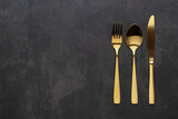 Gold knives, forks and spoons placed on a black background. Beautiful gold cutlery.