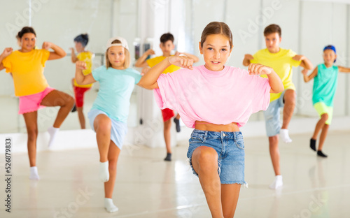 Portrait of preteen girl practicing hip-hop movements during group dance lesson in studio.