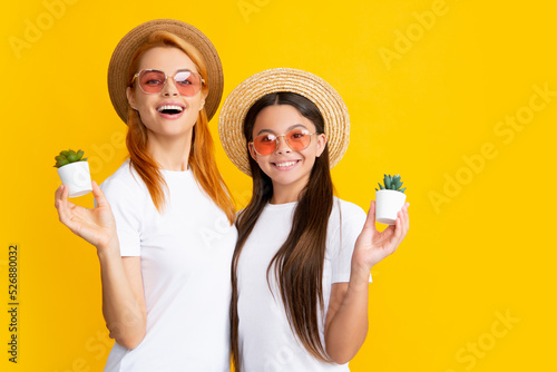 Happy woman mother and daughter child holding pot plant on yellow isoalted background.