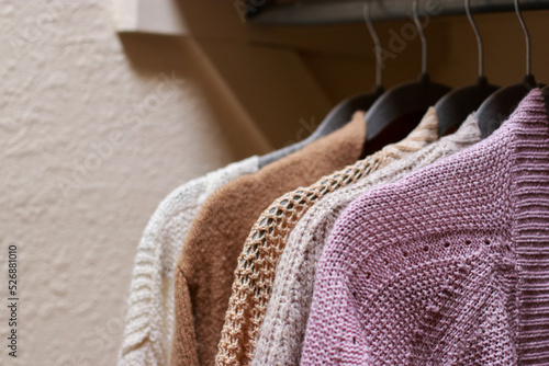 close up of pastel warm knitted cardigan sweater hanging in the closet. Cozy fall and winter wardrobe.