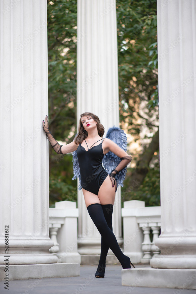 Beautiful girl with red lips in a black bodysuit, gloves and blue wings. Posing, leaning on a column Beautiful girl with red lips in a black bodysuit, gloves and blue wings. Posing, leaning on a column