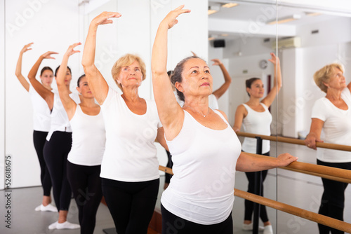 Women of different ages exercising ballet moves in training room. © JackF
