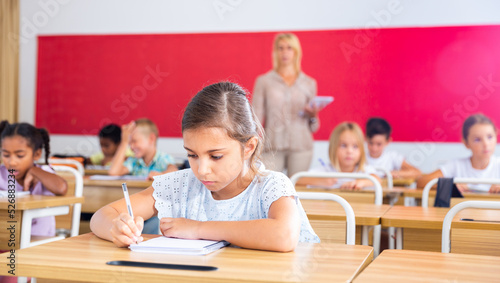 Portrait of diligent schoolgirl sitting in class working with classmates, writing exercise