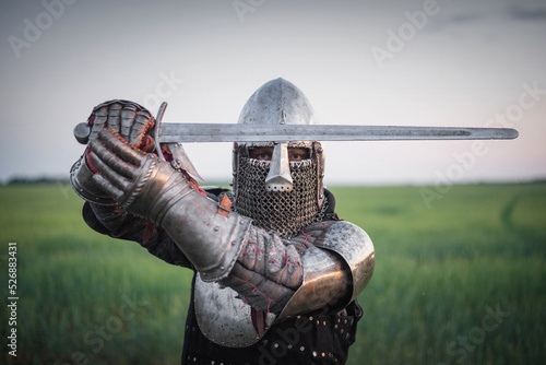 The knight in the plate armor and helmet holds a sword in hands close up Fototapet