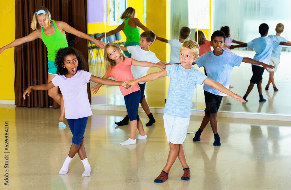 Group of glad cheerful positive smiling children practicing vigorous jive movements in dance class with female coach