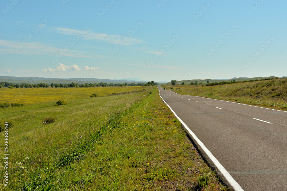 A straight asphalt road going through the endless hilly steppe on a warm summer day.