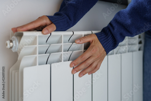 Closeup of woman warming her hands on the heater at home during cold winter days, top view. Female getting warm up her arms over radiator. Concept of heating season, cold weather. 